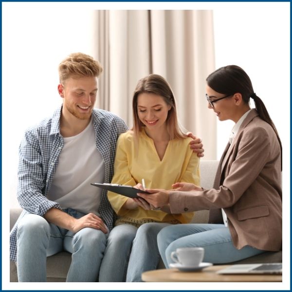 Young couple sitting with mortgage broker signing financial loan paperwork